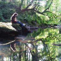 Woman sitting on rock by river looking at the reflections in the still water