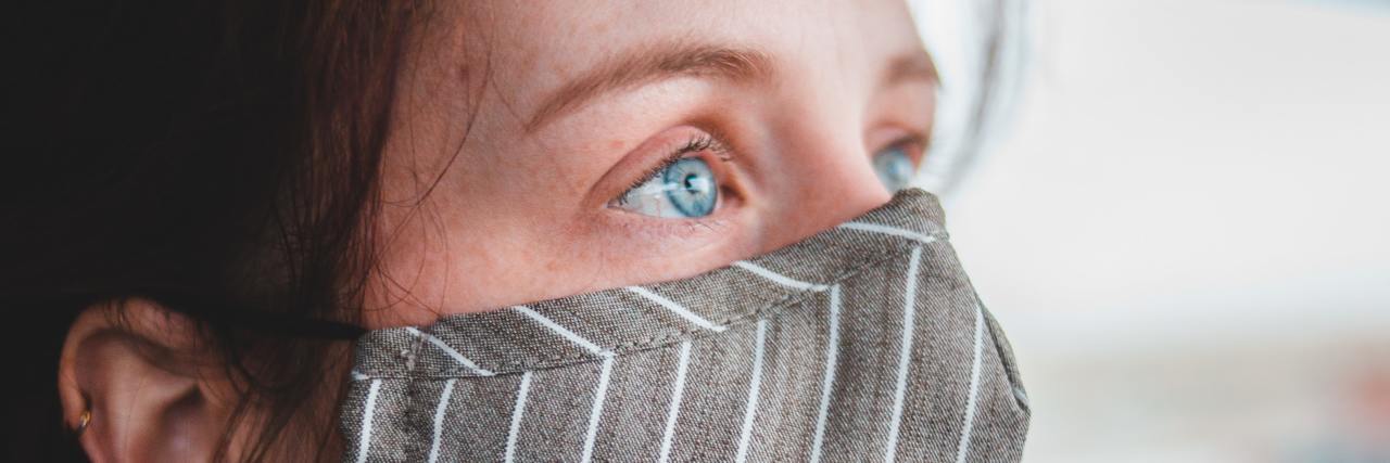 Why I'll Still Be Wearing My Mask Without the Mandate Woman wearing a striped face mask.