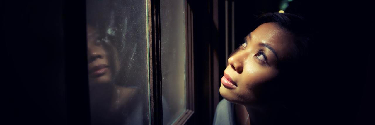 photo of a woman looking out of a window in fear
