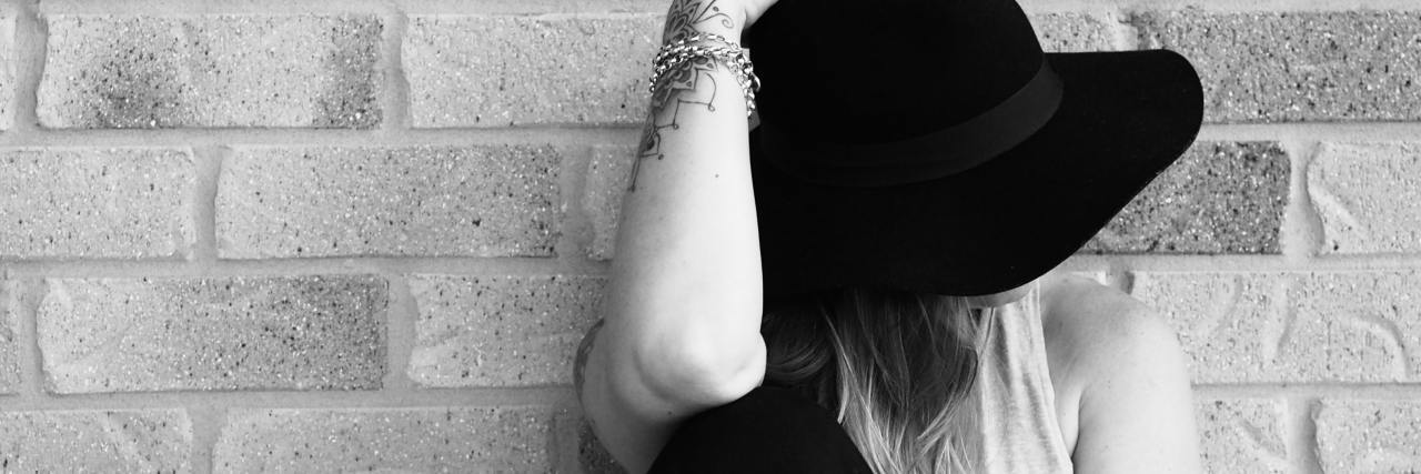 black and white photo of a woman against a brick wall with a black hat covering her face