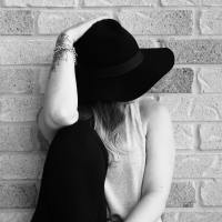 black and white photo of a woman against a brick wall with a black hat covering her face