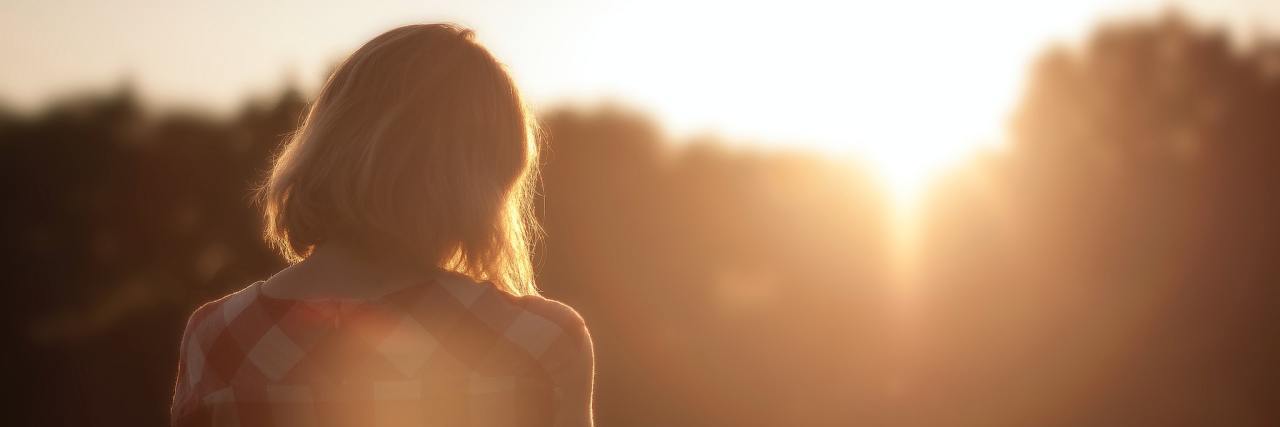 10 Things to Do When You Feel Hopeless About Your Illness A young woman with her back to the camera in a red flannel standing outside with the sun shining