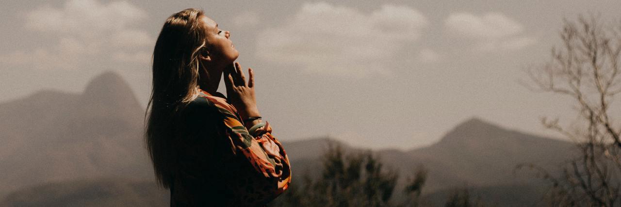 Dealing With Anxiety Manifesting as Anger During COVID-19 photo of a woman with her eyes closed and head raised with mountains behind her