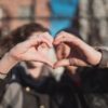 photo of two blurred people each making half a heart sign with their hands