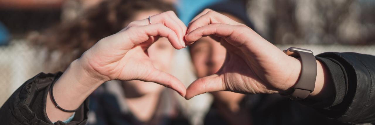 I Am My Hero, but My Mental Health Support Team Are My Sidekicks photo of two blurred people each making half a heart sign with their hands