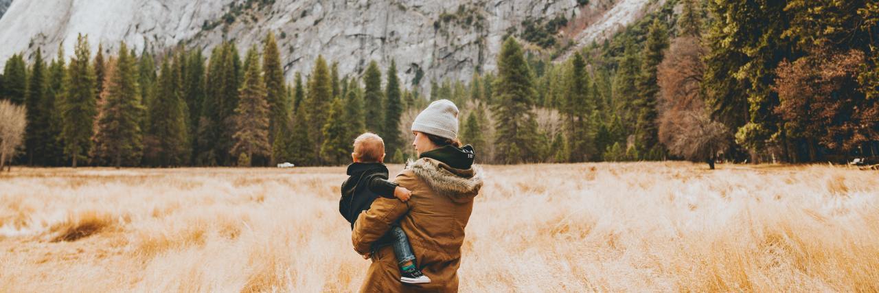 Read This if You're a New Mom Scared of Your Child Dying photo of a mother and child in a field with long yellow grass and mountains in distance