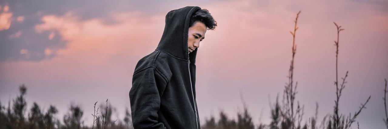 This Common Feeling Is Also My Biggest Trigger for a Depressive Episode photo of a man standing in a field around sunset, looking depressed or lonely