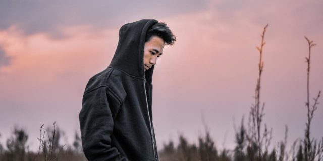 This Common Feeling Is Also My Biggest Trigger for a Depressive Episode photo of a man standing in a field around sunset, looking depressed or lonely