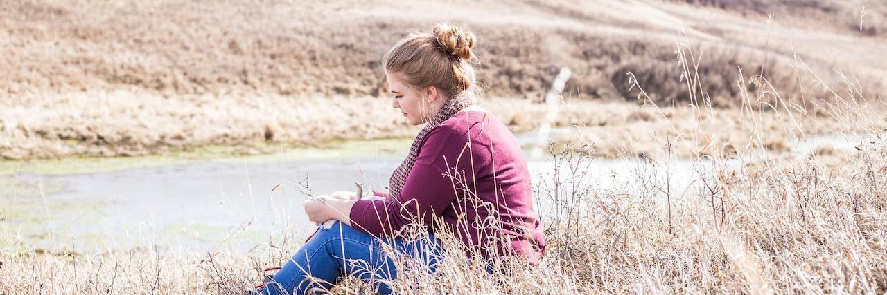 Woman sitting in field by river