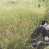 A white man in jeans and a flannel shirt sitting outside in a field with his dog