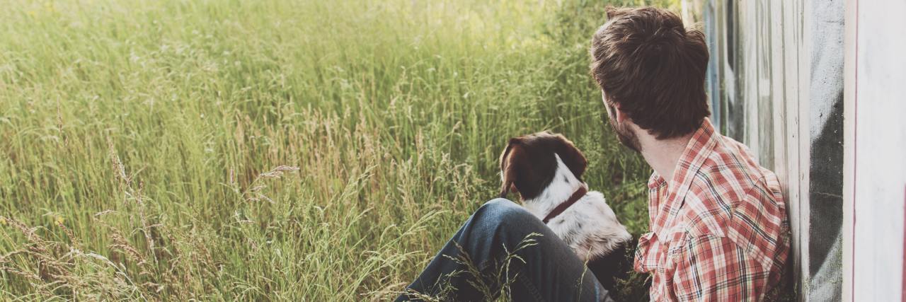 I Have Depression, but I'm Scared of Being Happy A white man in jeans and a flannel shirt sitting outside in a field with his dog