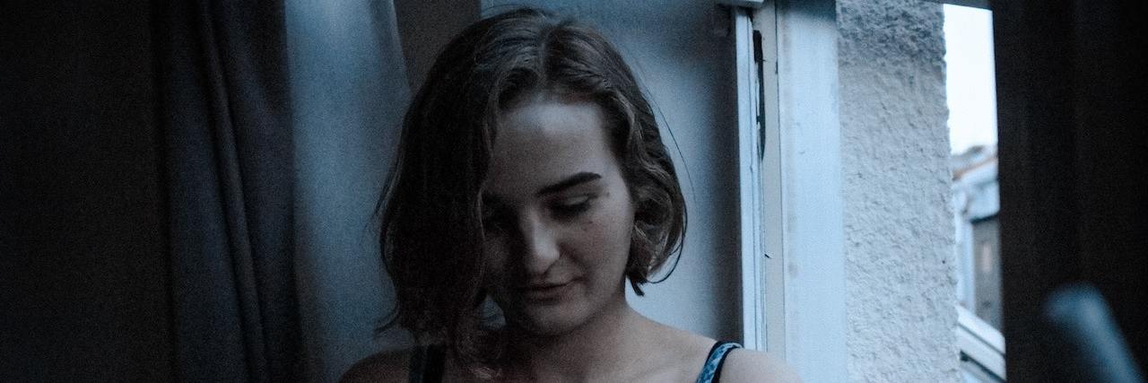 Surgery Saved My Life, But I Still Live With Chronic Illness Woman sitting by wooden bannister