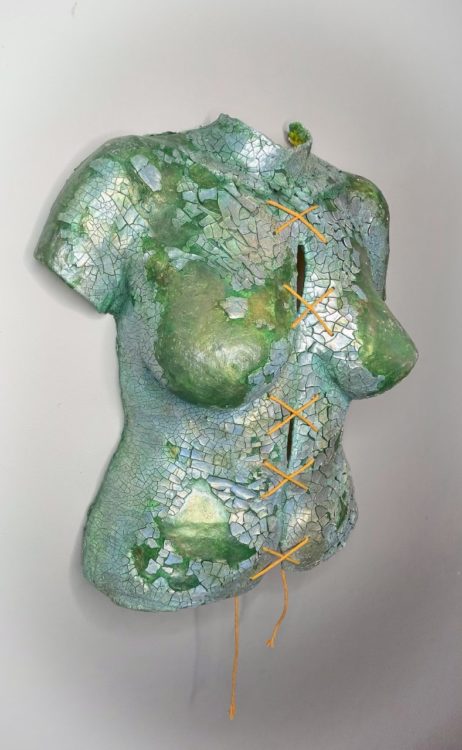 Body cast sculpture "Broken Body": torso and upper body in sea green color, covered in shining, cracked silvery pieces. String tied down the middle in a series making an "X" shape (shown from left angle)