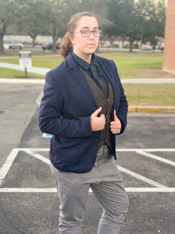 Author in high school: Person dressed in a blazer and grey pants, hair up with glasses, not smiling
