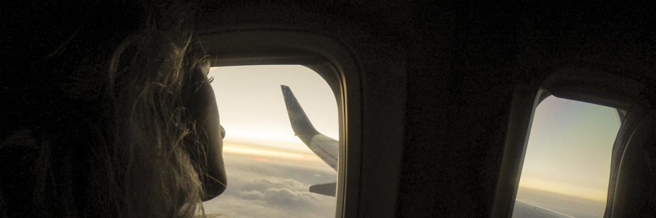 A young woman with long blonde hair looking out an airplane window