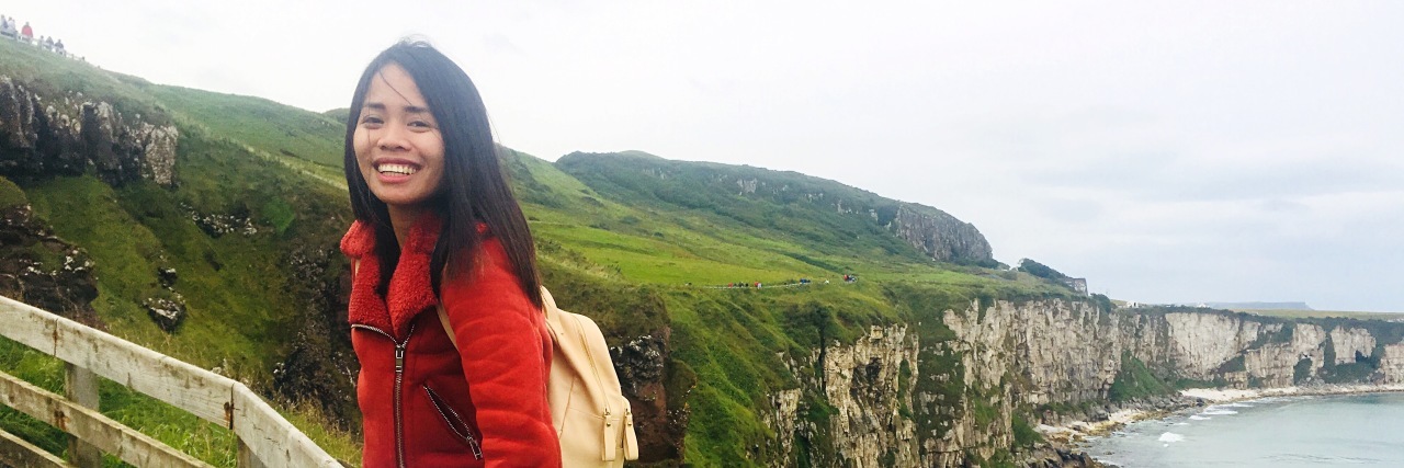 My Experience as a Teen Brain Injury Survivor Young woman sitting on a fence with ocean in background.