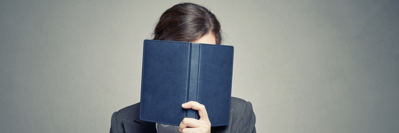 Is There a Link Between Introversion and Bipolar Disorder? A white businesswoman holding a blue book in front of her face