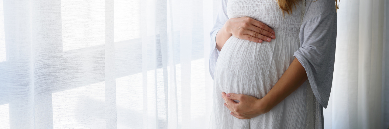 What Not to Say to Someone Who Is Chronically Ill and Pregnant Pregnant woman standing by window.