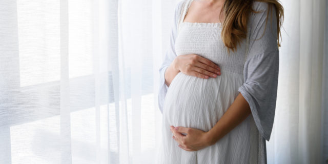 Pregnant woman standing by window.