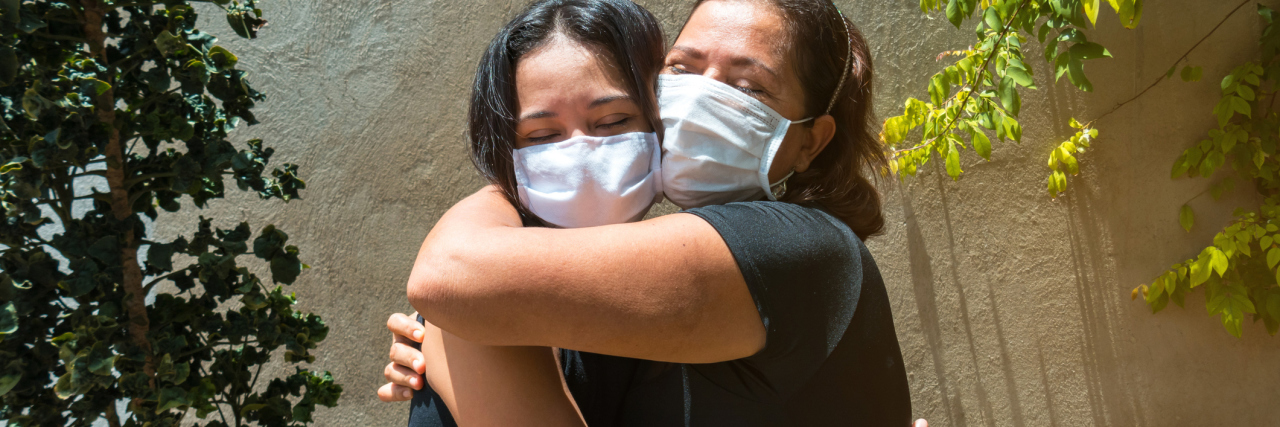 What to Say to Family and Friends After COVID-19 Vaccination Reunion photo of two women, one older, hugging and wearing face masks