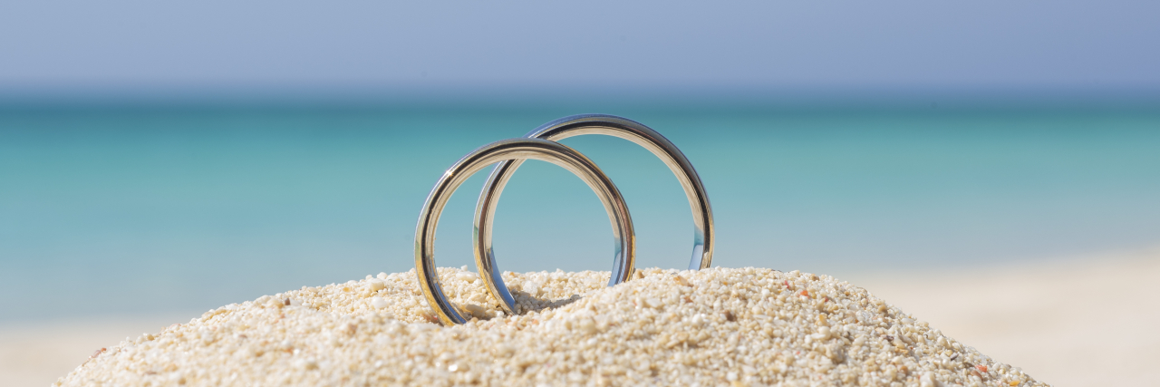Pair of wedding rings in sand on tropical beach