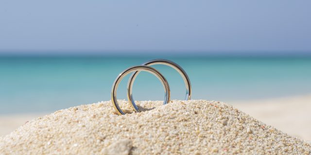 Why Many People With Disabilities Can't Have a Romantic June Wedding Pair of wedding rings in sand on tropical beach