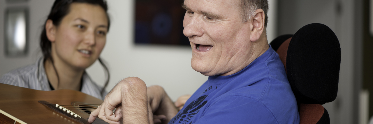 Why Biden's 'Caregiving Economy' Proposal Would Save Lives Man with disability playing guitar and woman looking on.