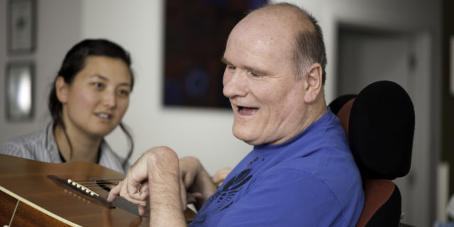 Why Biden's 'Caregiving Economy' Proposal Would Save Lives Man with disability playing guitar and woman looking on.