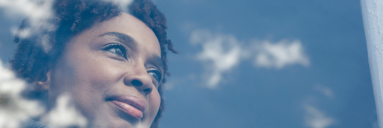 Photo of Black woman looking through glass with clouds reflected on it
