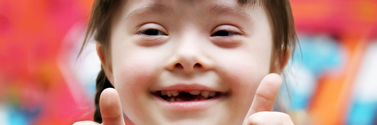 Let's Make 2021 a Year of Kindness for People With Down Syndrome Happy girl with Down syndrome giving thumbs up.