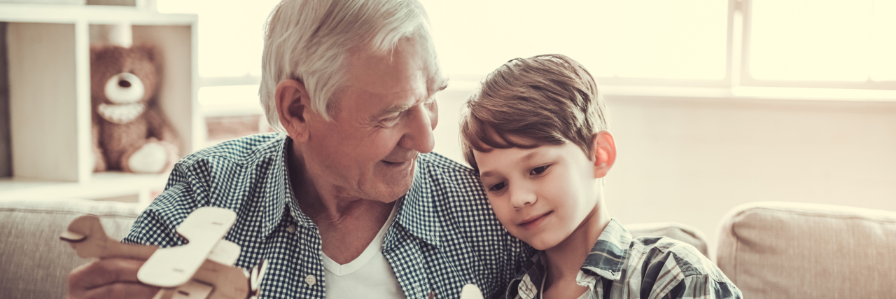 What It Was Like Watching My Grandfather's Alzheimer's Progress An older, white grandpa and his grandson playing with toy planes, smiling
