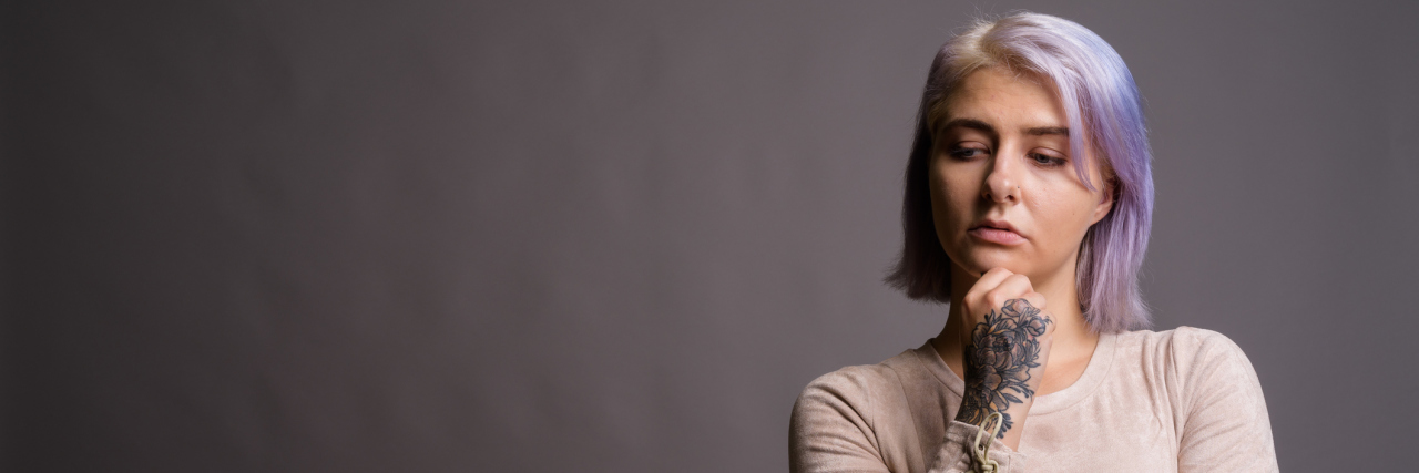 How My Ex-Therapist Used My Trauma to Gaslight Me A young white woman, with short purple hair against a gray background looking down