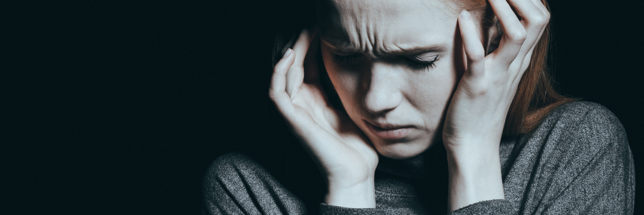 photo of a woman covering her ears with her hands against a dark background