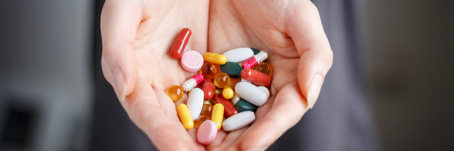 Hands holding pills of different colors and shapes