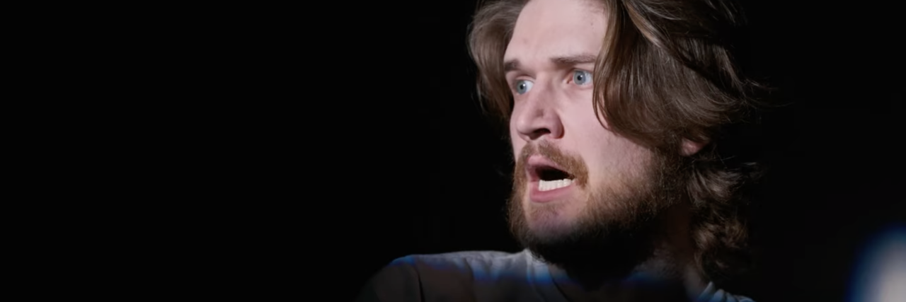 screenshot still from Netflix comedy special Bo Burnham: Inside, showing the comedian looking shocked with a light cast on him in otherwise darkness