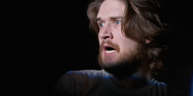 screenshot still from Netflix comedy special Bo Burnham: Inside, showing the comedian looking shocked with a light cast on him in otherwise darkness