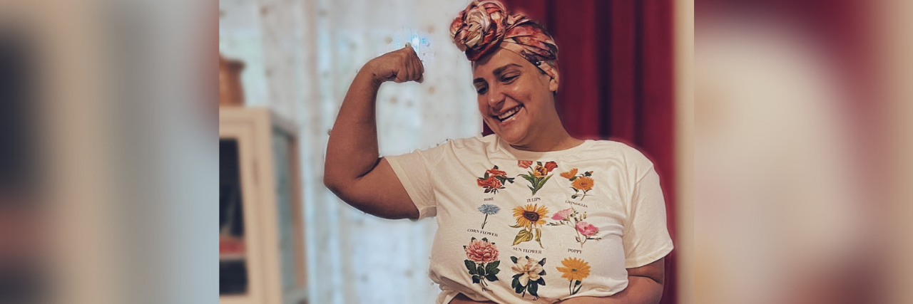 Author, a white woman wearing a cropped shirt showing off her "endo" belly, smiling and flexing her arm