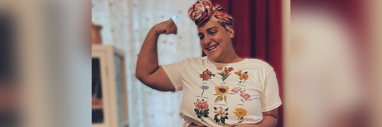 I'm Done Hiding My Chronic, Invisible Illness Author, a white woman wearing a cropped shirt showing off her "endo" belly, smiling and flexing her arm
