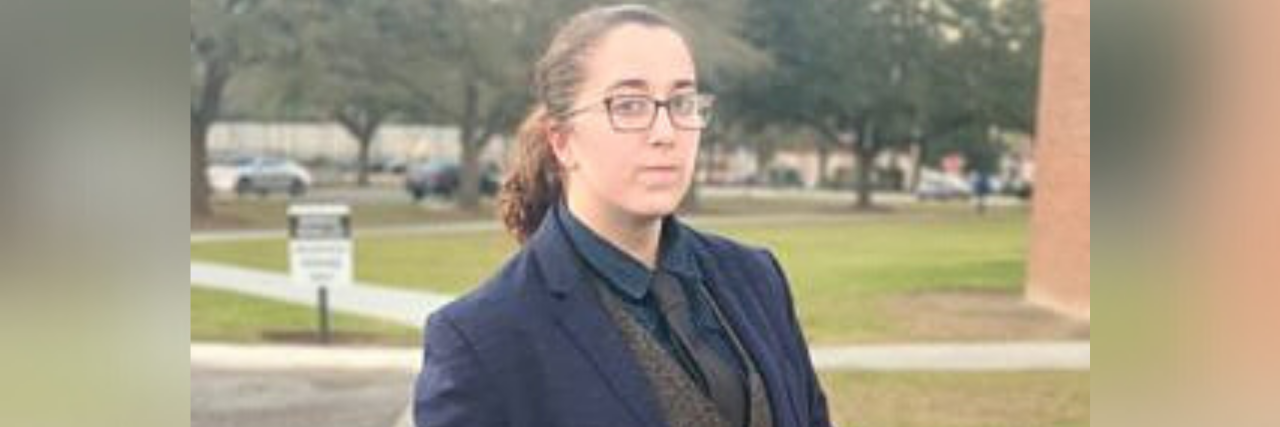 How I'm Recovering After Leaving a Homophobic Household Author in high school: Person dressed in a blazer and grey pants, hair up with glasses, not smiling