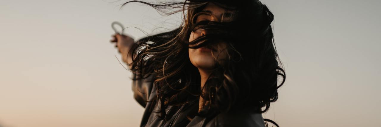 How It Feels to Finally Be Living My Authentic Gender Identity photo of a person at sunsrt in a field with hair across their face and arm outstretched behind him