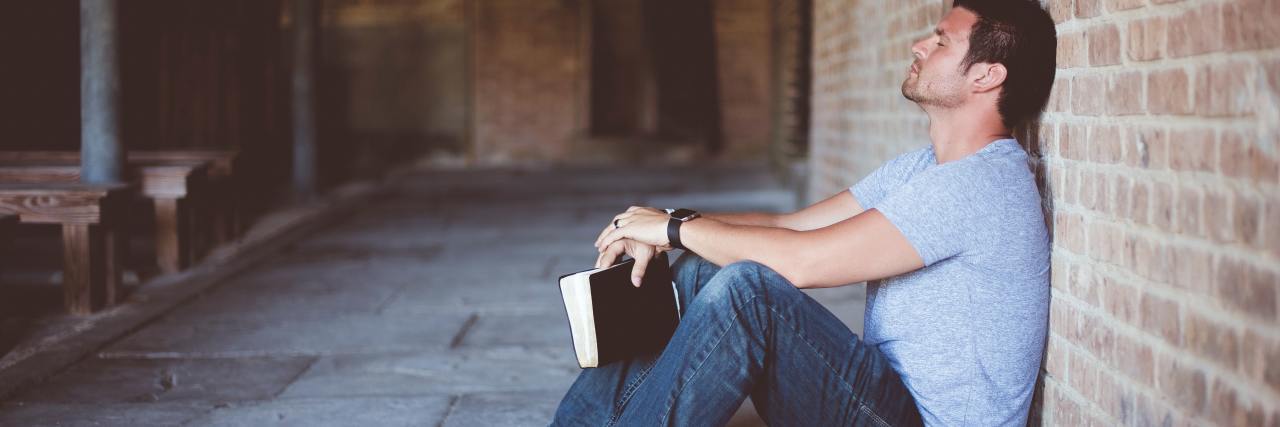 The Similarities Between Addiction Recovery and the Catholic Church photo of a man leaning against a wall holding a black book in his hands