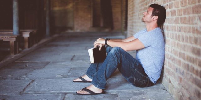 How the Addiction Recovery World is Like the Catholic Church photo of a man leaning against a wall holding a black book in his hands