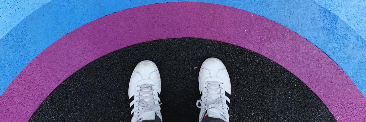 A person standing near the LGBTQIA+ rainbow