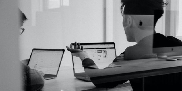 black and white photo of two people talking in a meeting with laptops