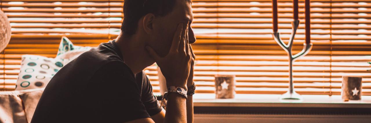 Dear Men: Keeping Our Emotions Hidden Is Harming Our Mental Health photo of a man sitting on a bed in front of window with his hands covering his face