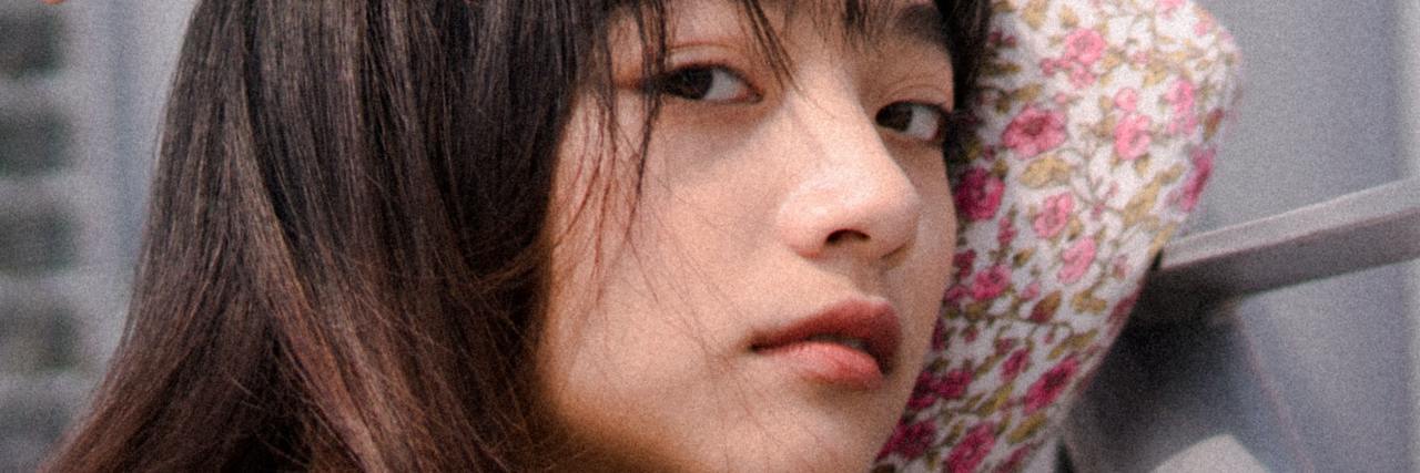Read This If You're Anxious About COVID-19 Lockdown Ending photo of a young woman in in floral dress looking into camera while leaning on wall