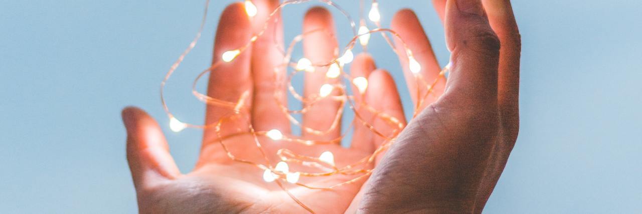 photo of someone's hands holding string lights up against sky