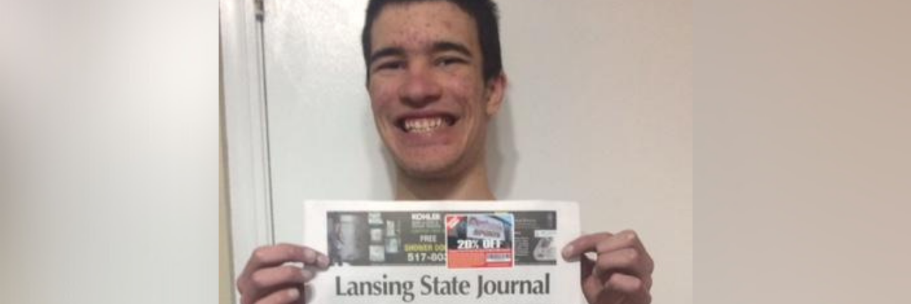 Dominic holding up a newspaper with his article on the front page.