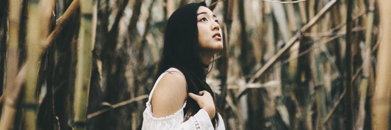 The Asian and Pacific Islander Community Needs to Change Its Mental Health Narrative photo of a woman standing among bare trees, looking upset