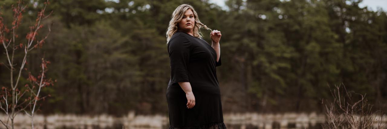 photo of a plus-size woman with a backdrop of trees, looking into camera with serious expression